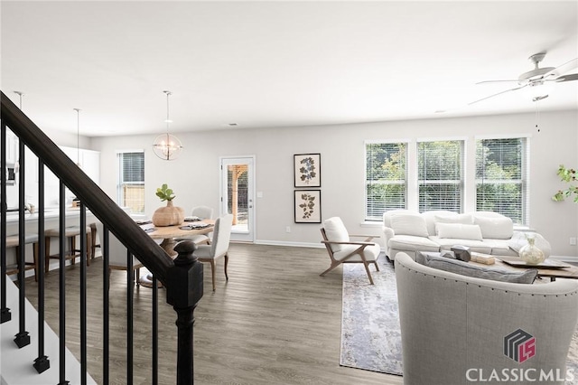 living room with baseboards, wood finished floors, stairs, and ceiling fan with notable chandelier