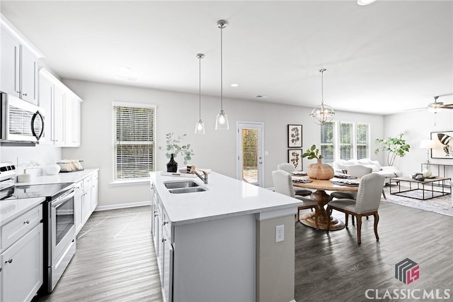 kitchen featuring open floor plan, an island with sink, light countertops, stainless steel appliances, and a sink