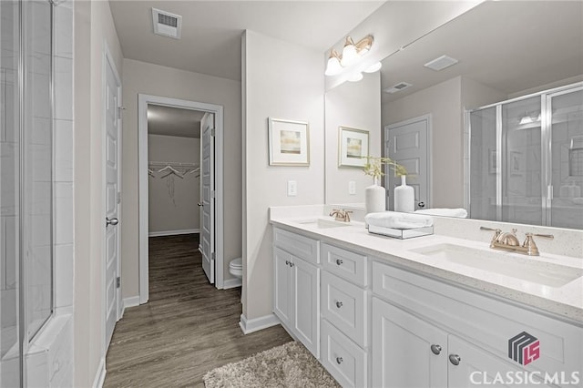 bathroom featuring a sink, visible vents, a shower with door, and toilet