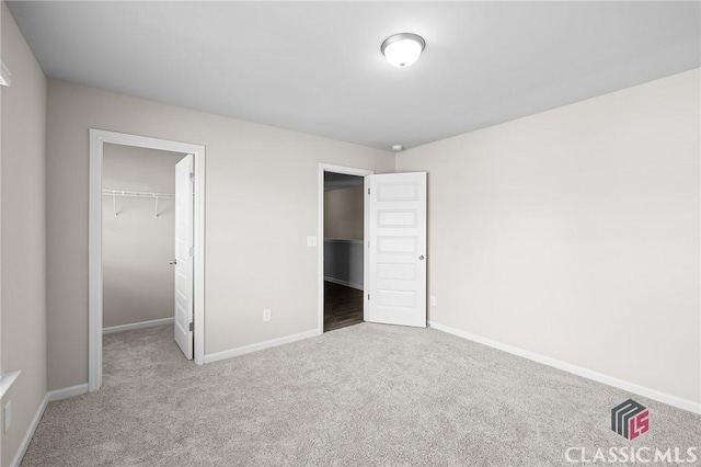 unfurnished bedroom with a closet, baseboards, a spacious closet, and carpet flooring