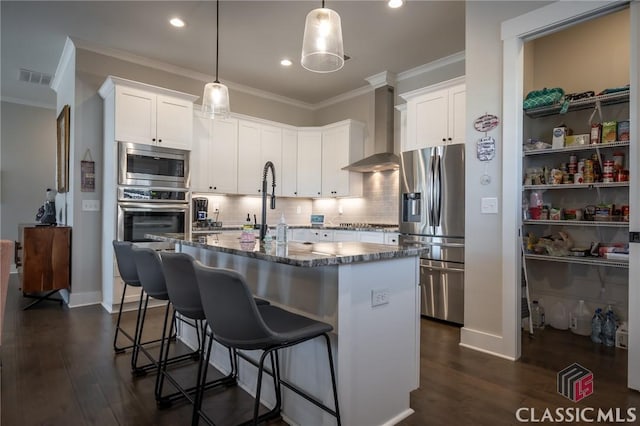 kitchen featuring white cabinetry, stainless steel appliances, wall chimney exhaust hood, and a center island with sink