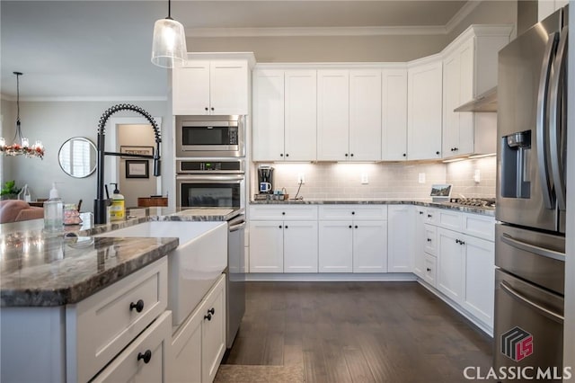 kitchen featuring white cabinetry, dark stone countertops, stainless steel appliances, ornamental molding, and decorative light fixtures