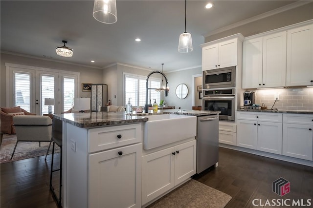 kitchen with hanging light fixtures, a kitchen breakfast bar, stainless steel appliances, an island with sink, and white cabinets