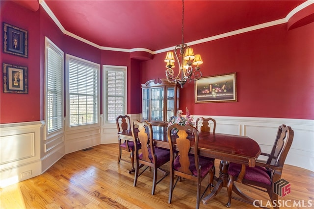 dining area with ornamental molding, an inviting chandelier, and light hardwood / wood-style floors