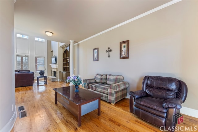 living room with decorative columns, ornamental molding, a fireplace, and light hardwood / wood-style flooring