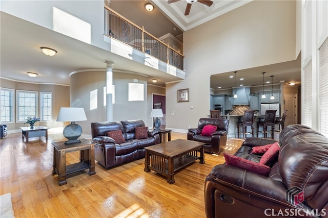 living room with ceiling fan, ornamental molding, light hardwood / wood-style floors, and a towering ceiling