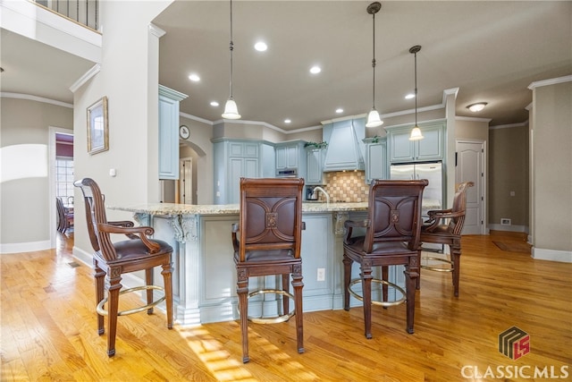 kitchen with blue cabinetry, tasteful backsplash, light stone countertops, light hardwood / wood-style floors, and decorative light fixtures