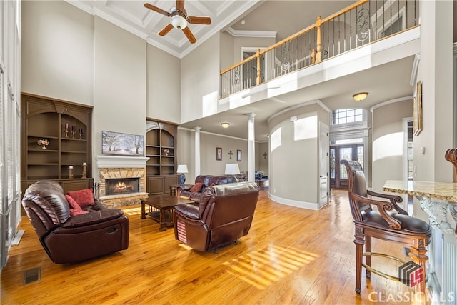 living room featuring a fireplace, decorative columns, ceiling fan, crown molding, and light wood-type flooring