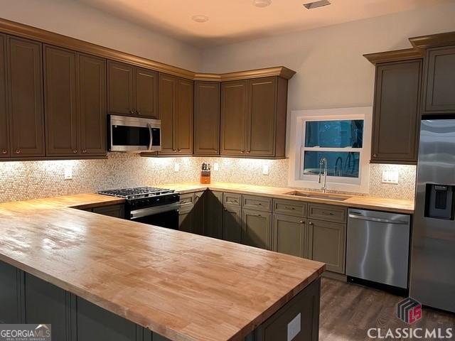 kitchen featuring sink, wooden counters, appliances with stainless steel finishes, decorative backsplash, and kitchen peninsula