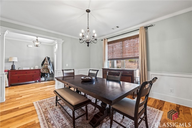 dining area featuring a notable chandelier, crown molding, light wood-type flooring, and ornate columns