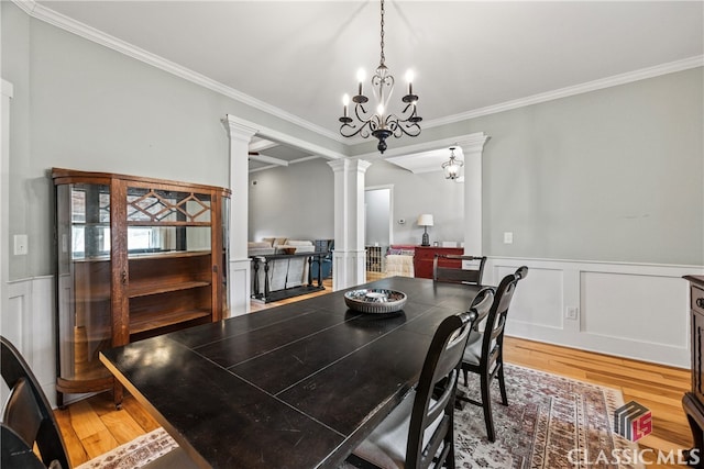 dining space with crown molding, a notable chandelier, hardwood / wood-style flooring, and ornate columns