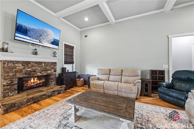 living room featuring coffered ceiling, a stone fireplace, light hardwood / wood-style flooring, ornamental molding, and beamed ceiling