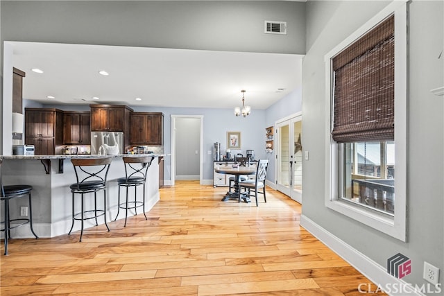 kitchen featuring stainless steel refrigerator, a kitchen bar, a notable chandelier, light hardwood / wood-style floors, and dark brown cabinets