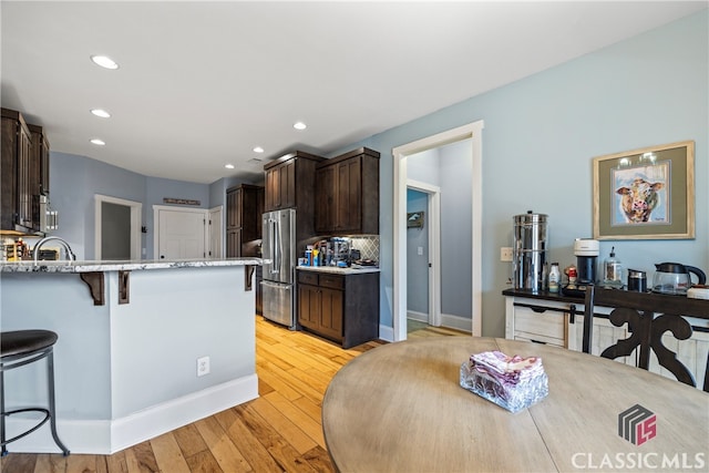 kitchen with dark brown cabinetry, tasteful backsplash, light hardwood / wood-style flooring, appliances with stainless steel finishes, and a kitchen breakfast bar