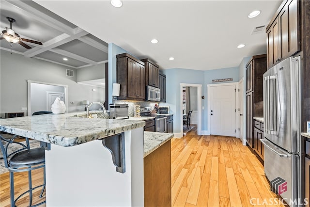 kitchen with appliances with stainless steel finishes, light stone counters, a kitchen breakfast bar, and kitchen peninsula