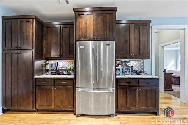 kitchen featuring high quality fridge, light stone countertops, dark brown cabinets, and light hardwood / wood-style flooring