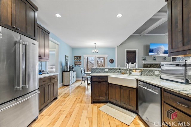 kitchen featuring decorative light fixtures, sink, dark brown cabinetry, stainless steel appliances, and light hardwood / wood-style flooring