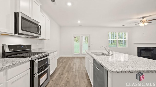 kitchen with appliances with stainless steel finishes, sink, white cabinets, a kitchen island with sink, and light stone countertops