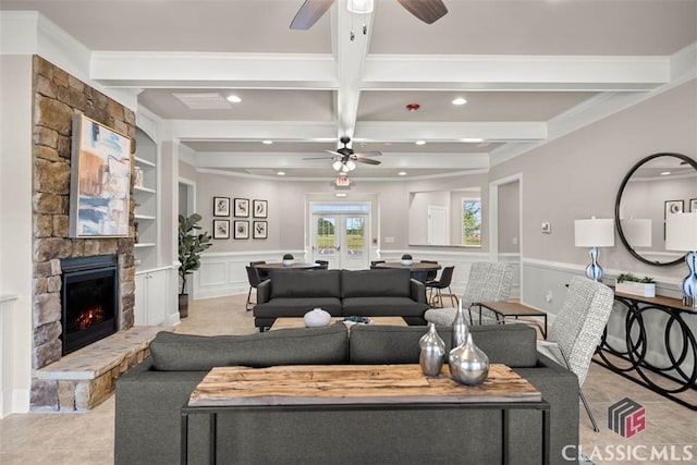 living room with french doors, built in shelves, a stone fireplace, ornamental molding, and beam ceiling