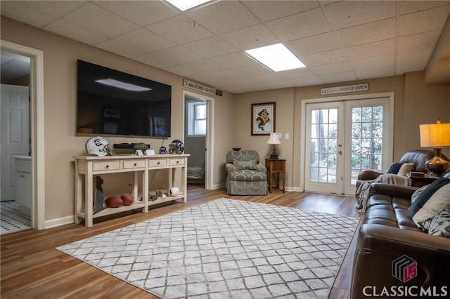 living room with a drop ceiling, light wood-type flooring, and french doors