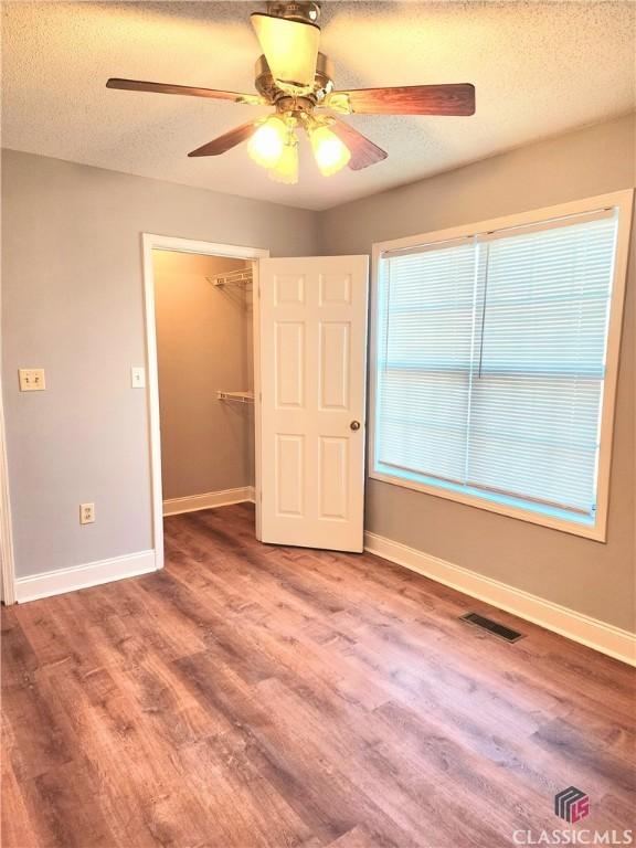 unfurnished bedroom with hardwood / wood-style flooring, ceiling fan, a textured ceiling, a walk in closet, and a closet