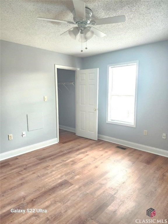 unfurnished bedroom with wood-type flooring, ceiling fan, a textured ceiling, and a closet