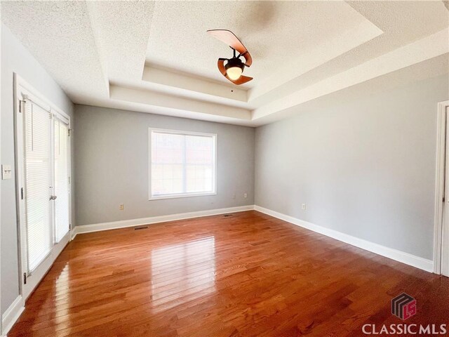 empty room with ceiling fan, wood-type flooring, a tray ceiling, and a textured ceiling