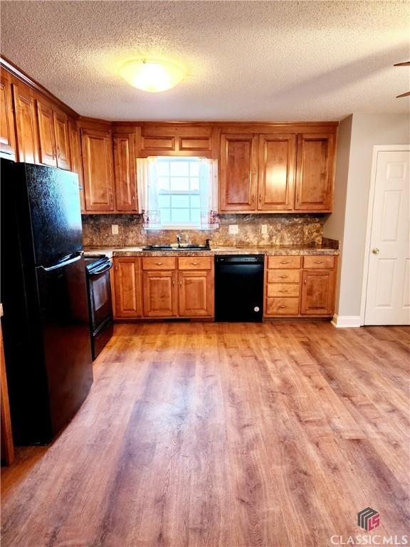 kitchen featuring sink, decorative backsplash, light hardwood / wood-style flooring, and black appliances