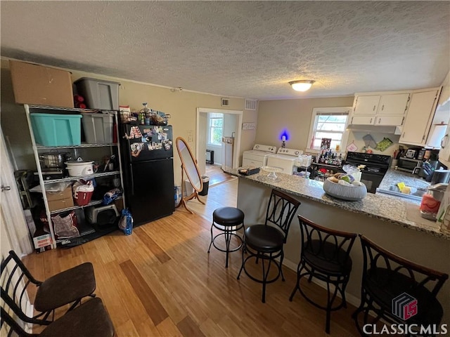 kitchen with light stone counters, washer and dryer, light wood-type flooring, a wealth of natural light, and black appliances