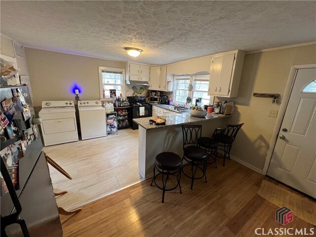 kitchen with separate washer and dryer, light hardwood / wood-style flooring, kitchen peninsula, black range with electric cooktop, and dark stone counters