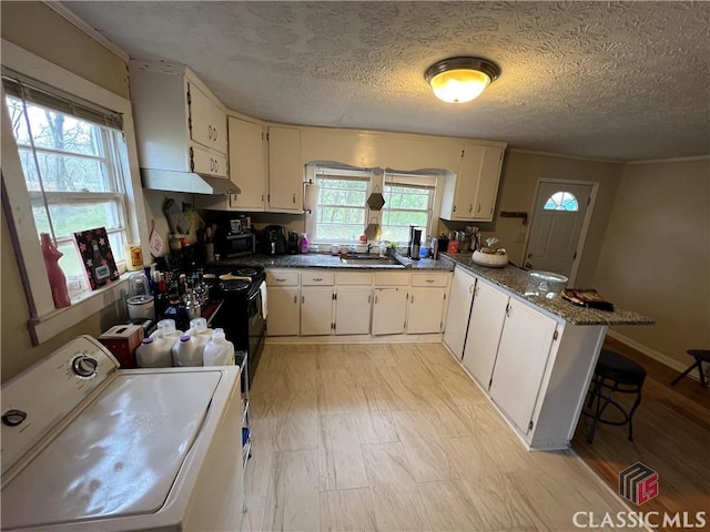 kitchen with a healthy amount of sunlight, washer / dryer, kitchen peninsula, and dark stone countertops