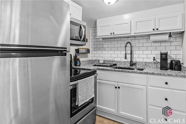 kitchen with appliances with stainless steel finishes, white cabinetry, sink, decorative backsplash, and light stone countertops