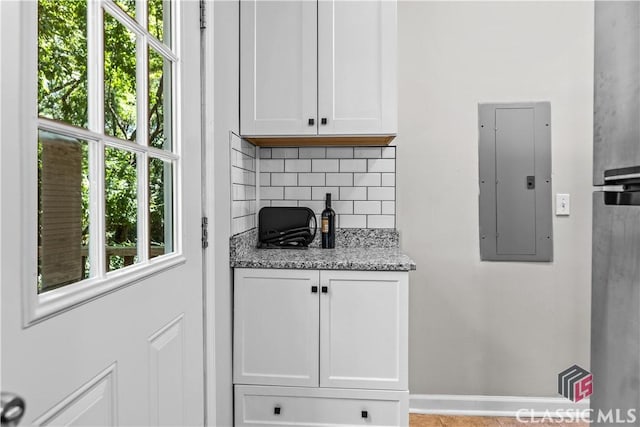 kitchen featuring white cabinetry, decorative backsplash, electric panel, and light stone counters