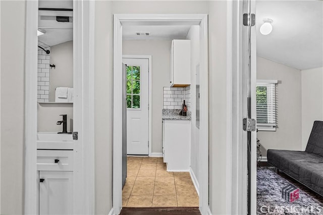 hall with lofted ceiling, sink, and light tile patterned floors