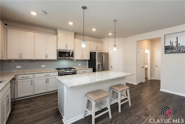 kitchen featuring dark hardwood / wood-style floors, hanging light fixtures, a center island, light stone counters, and stainless steel appliances