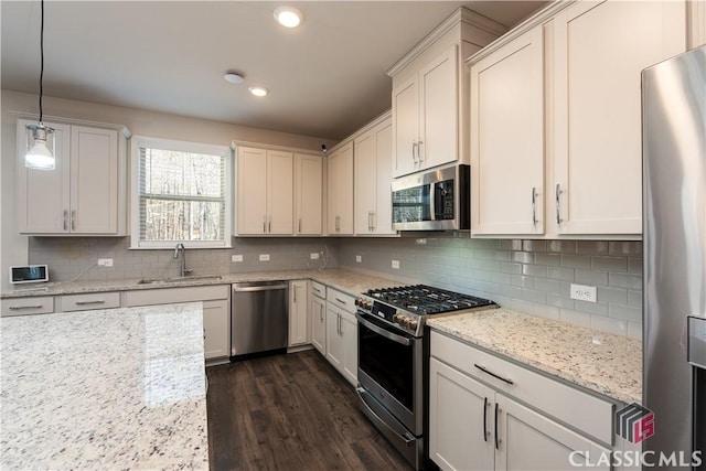 kitchen featuring sink, light stone counters, decorative light fixtures, appliances with stainless steel finishes, and white cabinets