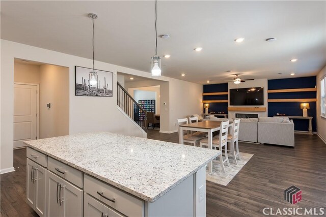 kitchen with dark hardwood / wood-style floors, decorative light fixtures, light stone countertops, and a kitchen island