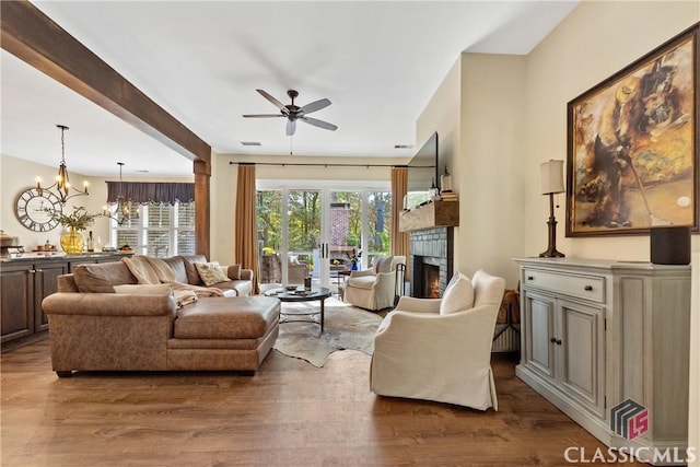 living room with wood-type flooring, a brick fireplace, and ceiling fan with notable chandelier