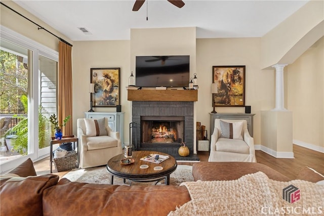 living room featuring ceiling fan, hardwood / wood-style floors, decorative columns, and a brick fireplace