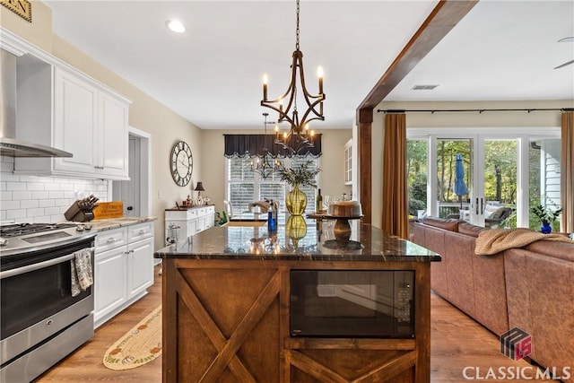 kitchen with wall chimney range hood, white cabinetry, a kitchen island, stainless steel range with gas cooktop, and dark stone counters