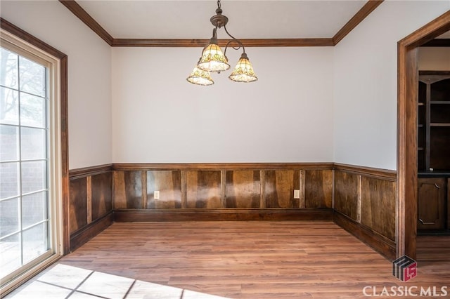 unfurnished dining area featuring crown molding, wood-type flooring, and an inviting chandelier