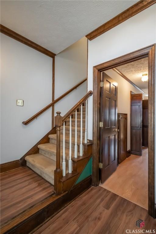 stairs featuring wood-type flooring, ornamental molding, and a textured ceiling