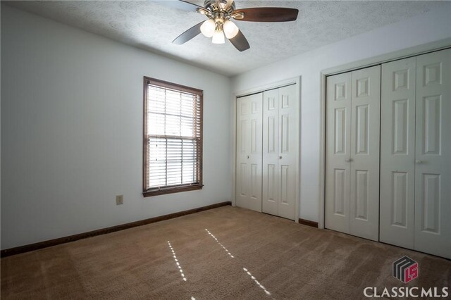 unfurnished bedroom featuring multiple closets, light colored carpet, a textured ceiling, and ceiling fan