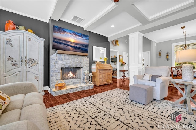 living room featuring crown molding, hardwood / wood-style flooring, a stone fireplace, beamed ceiling, and ornate columns