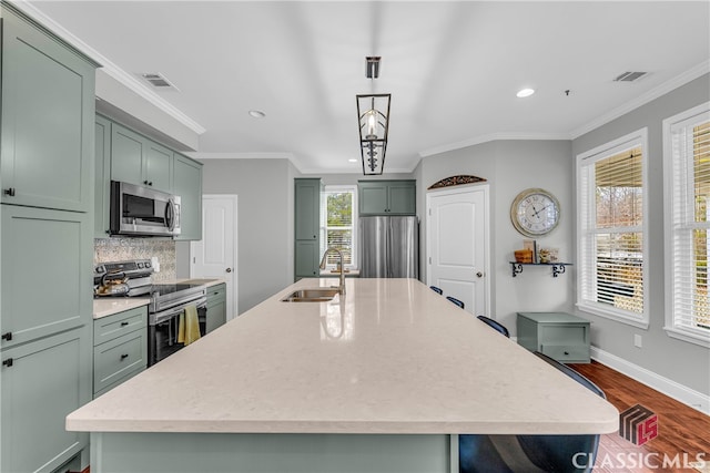 kitchen with sink, green cabinetry, decorative light fixtures, appliances with stainless steel finishes, and an island with sink