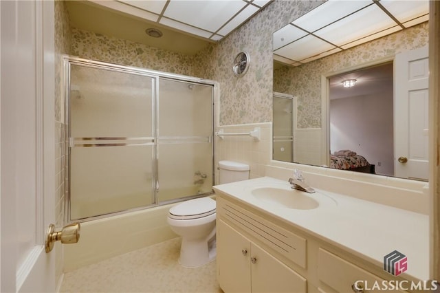 full bathroom featuring toilet, vanity, shower / bath combination with glass door, and tile walls