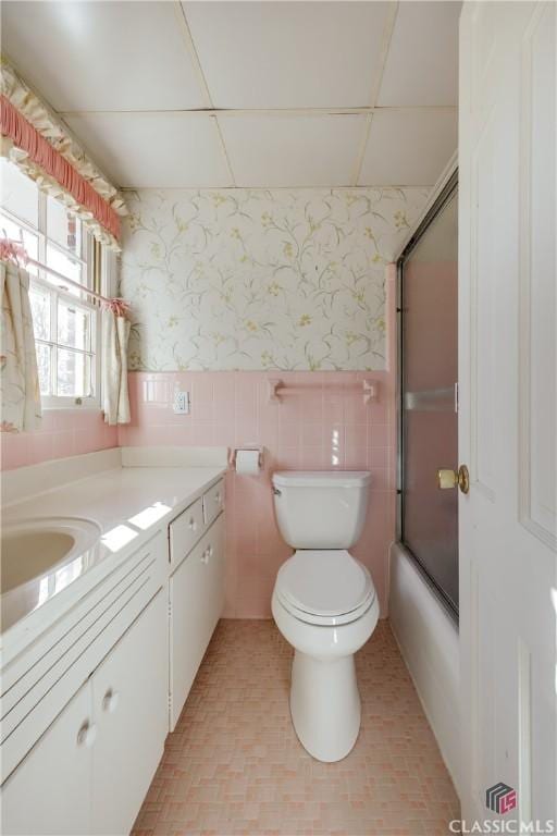 full bathroom featuring vanity, combined bath / shower with glass door, tile walls, and toilet