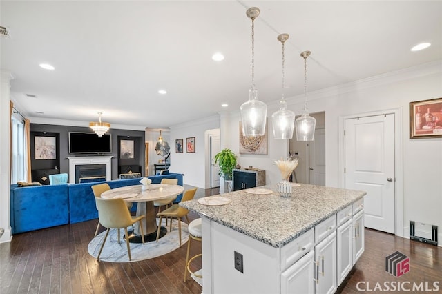 kitchen featuring light stone counters, white cabinets, a center island, and hanging light fixtures