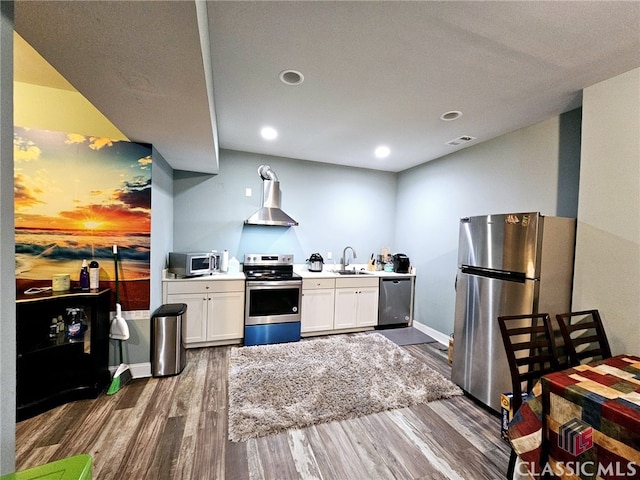 kitchen with stainless steel appliances, wall chimney range hood, dark hardwood / wood-style flooring, sink, and white cabinetry