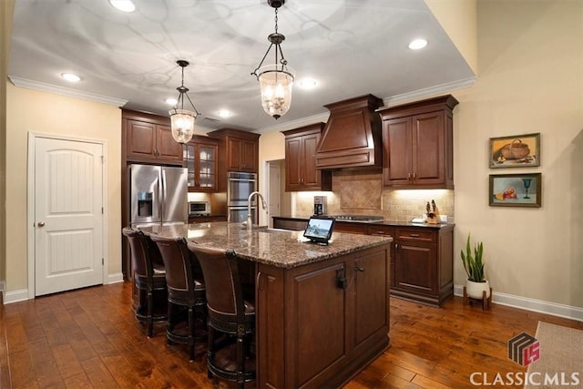 kitchen with premium range hood, sink, decorative light fixtures, a center island with sink, and appliances with stainless steel finishes